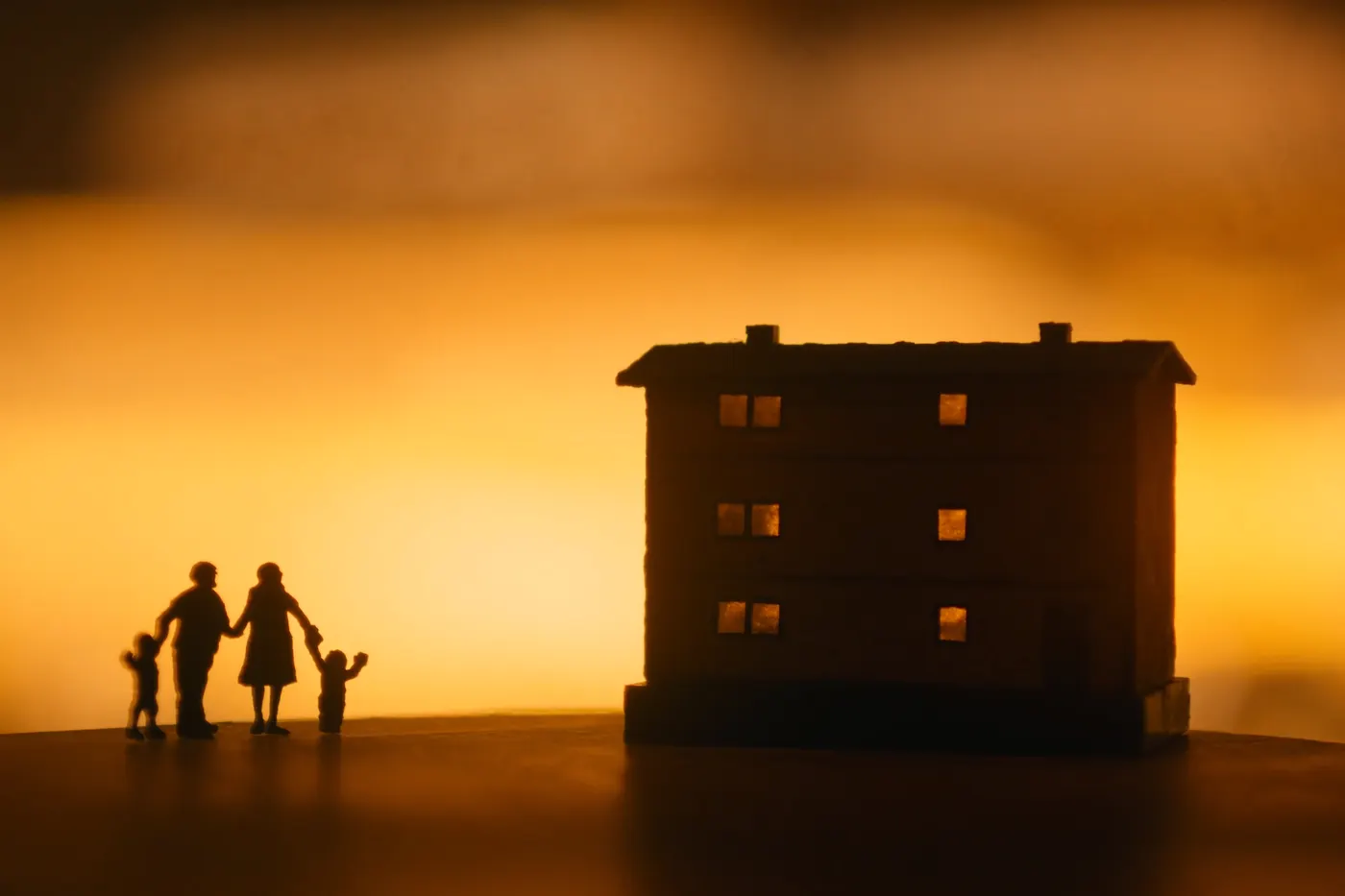 A silhouetted family beside a glowing home at sunset