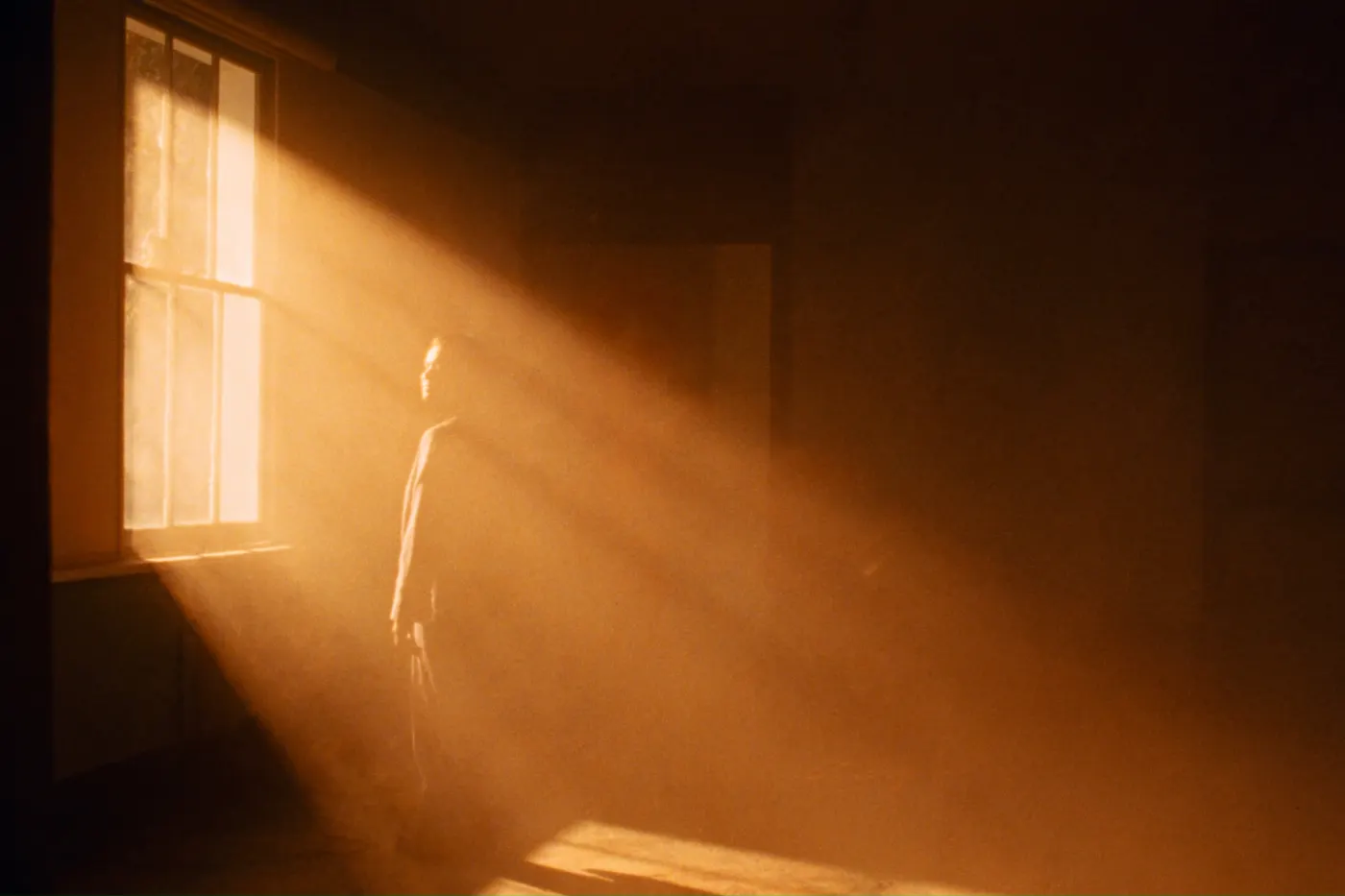 A figure standing in a room filled with warm streaming light