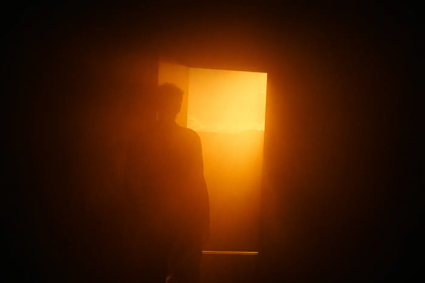 A lone figure at a doorway filled with warm golden light